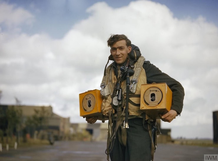 Wireless operator of an Avro Lancaster bomber carrying two pigeon boxes. carrying pigeons in boxes. Wikimedia Commons.